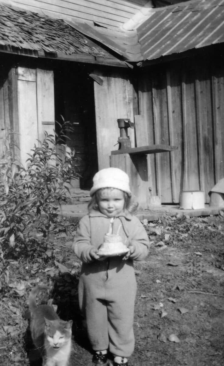 Archival photo of a child holding a small cake in the family yard