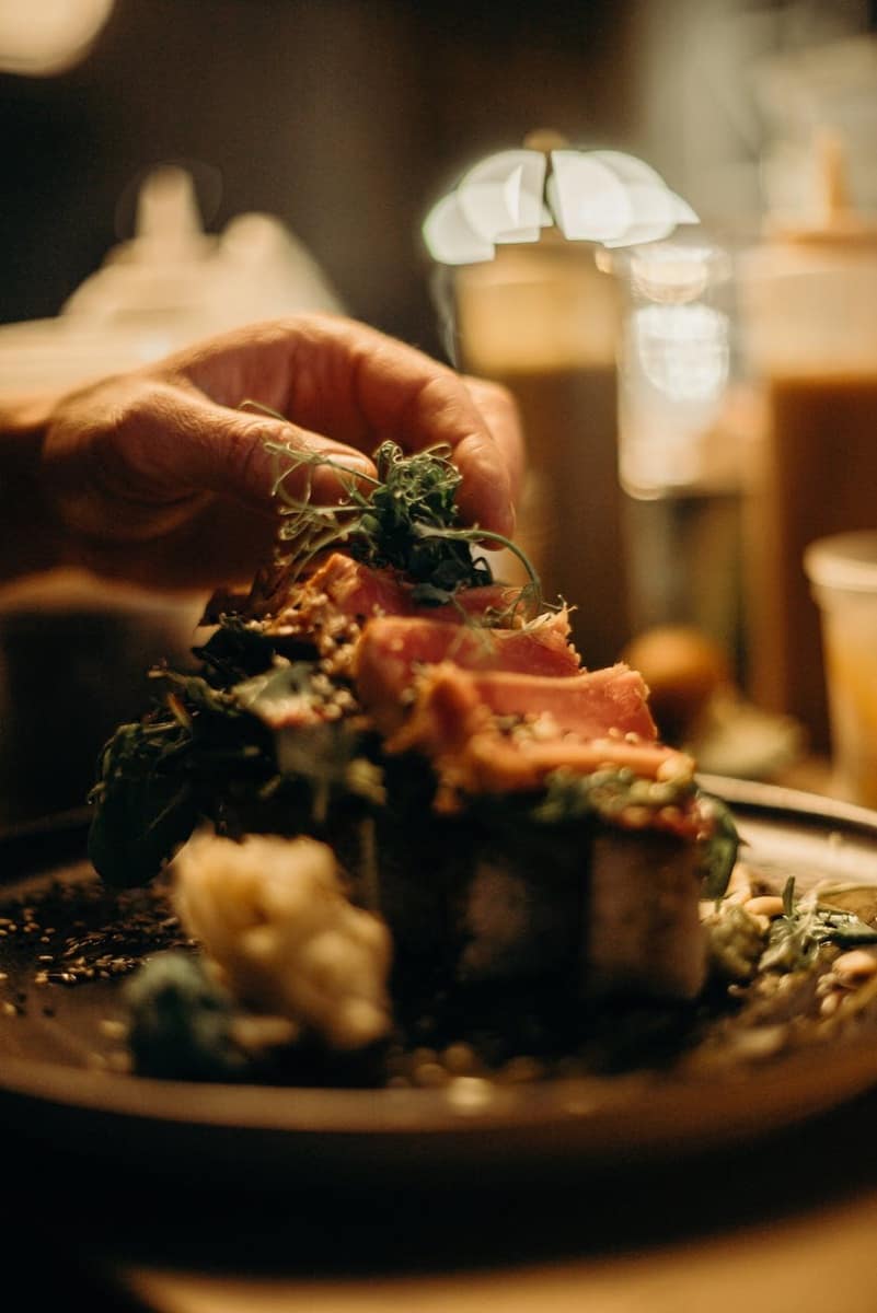 Hands garnishing a plated dish with fresh herbs