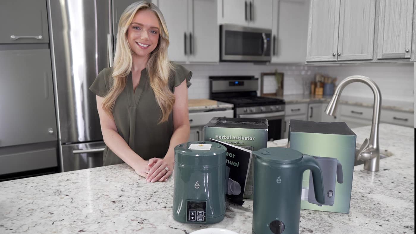 Host holding the ÉCRU Green 2oz decarboxylator in a bright home kitchen