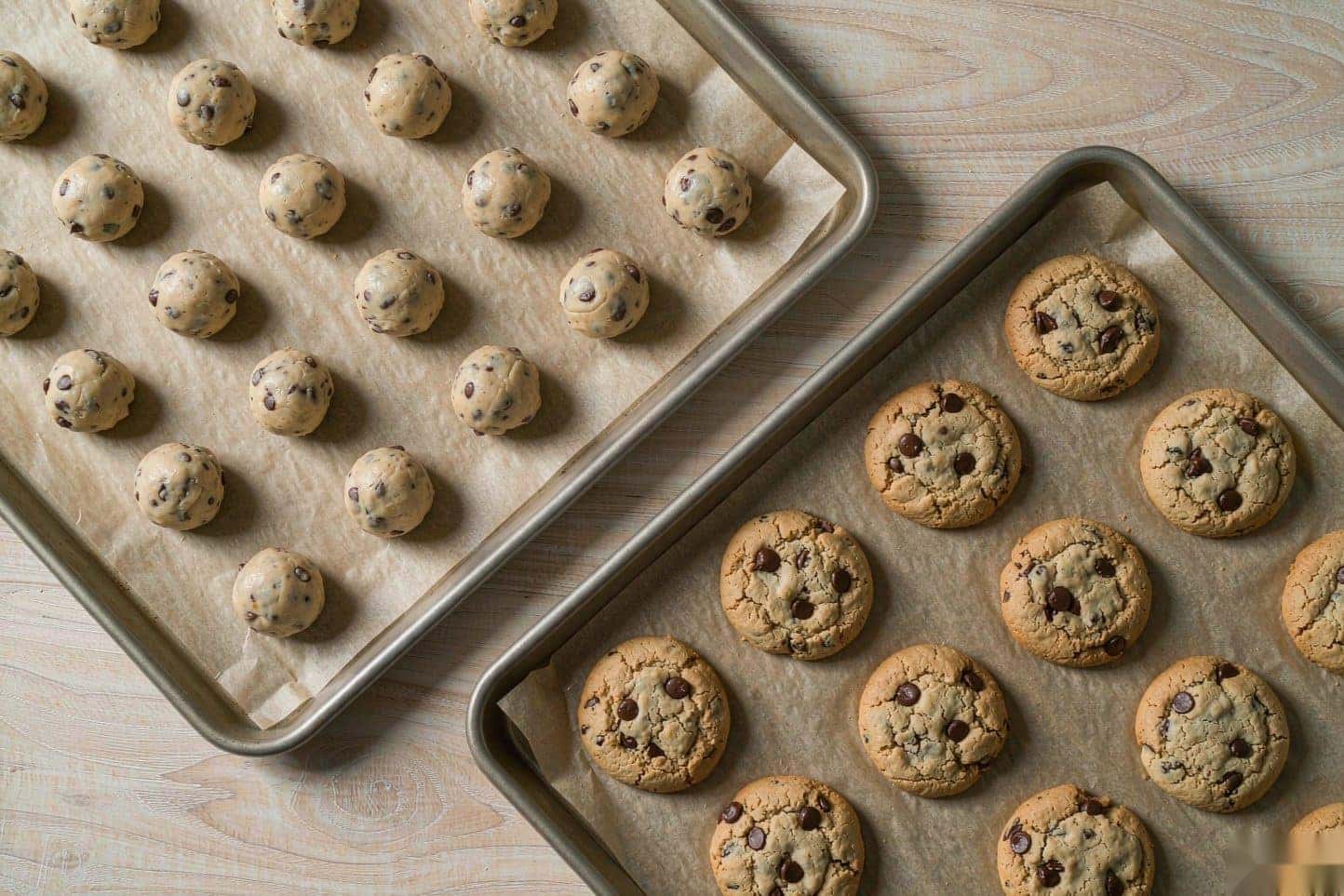 Two baking sheets, one with evenly scooped cookie dough balls and one with baked chocolate chip cookies