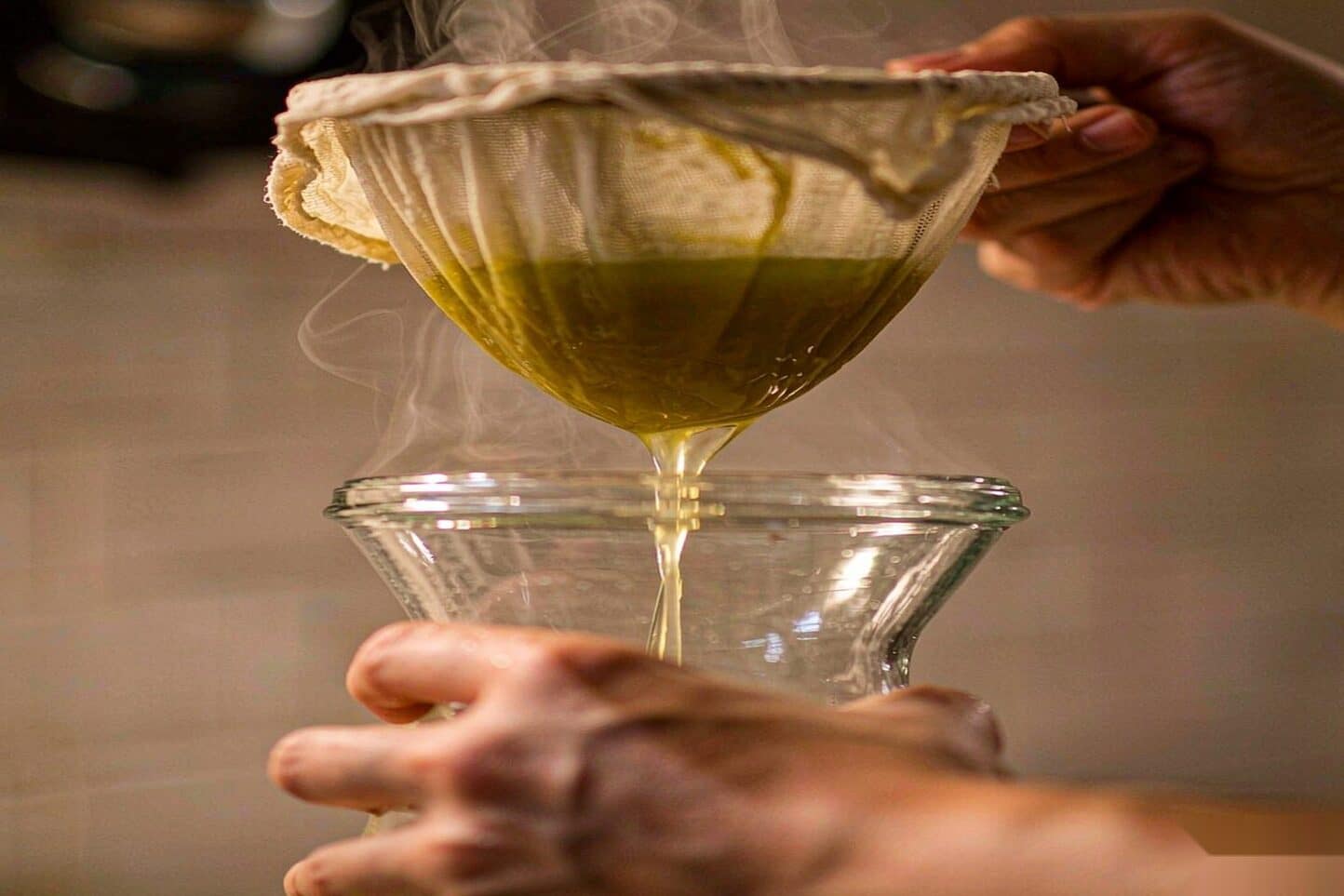 Cannabutter being strained through cheesecloth into a glass jar