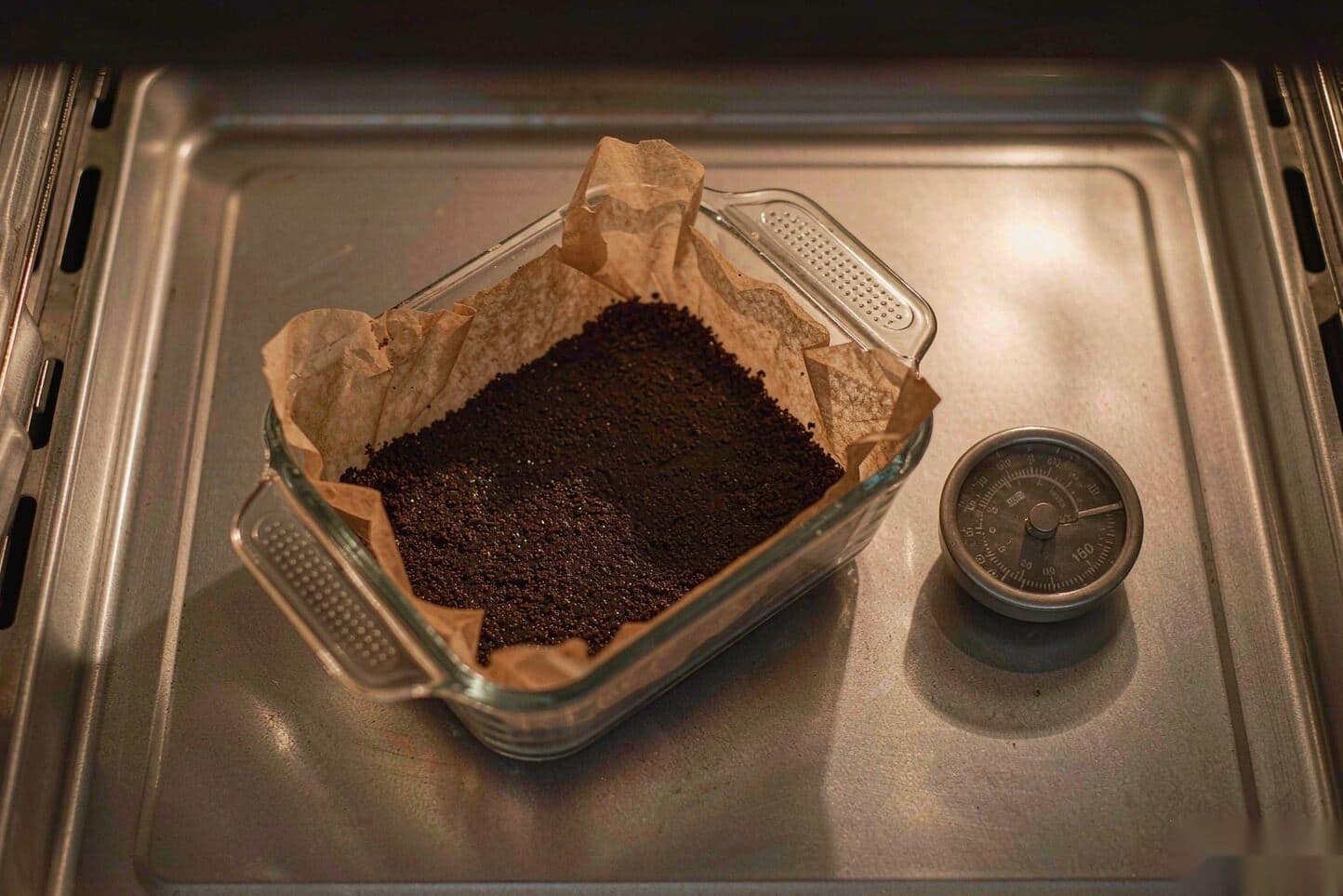 Hash spread in a thin layer on parchment in an oven-safe glass dish with an oven thermometer