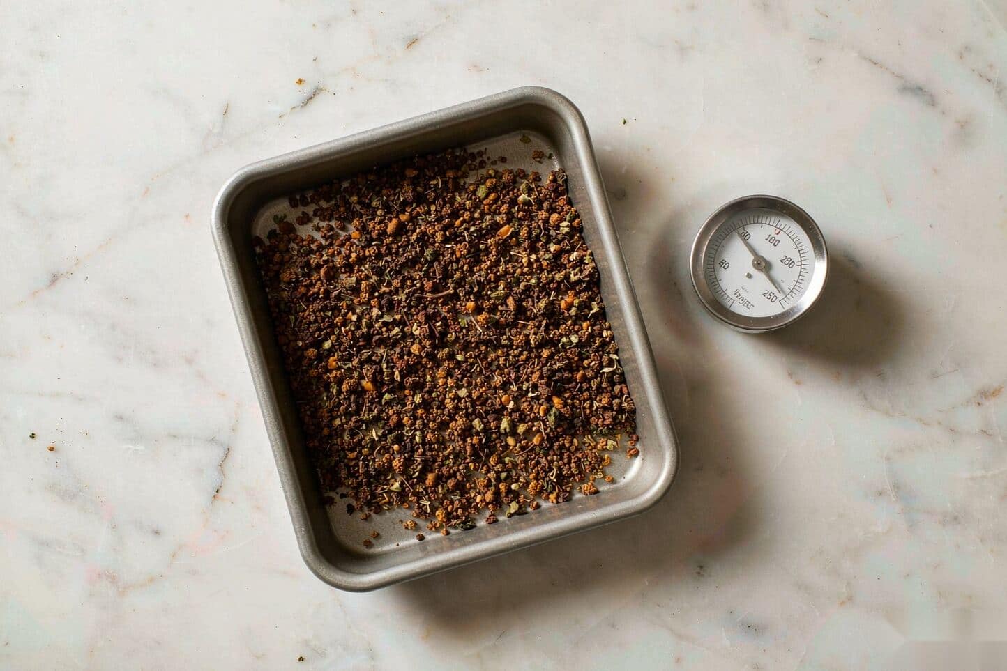 Ground cannabis spread in a thin layer on parchment with an oven thermometer