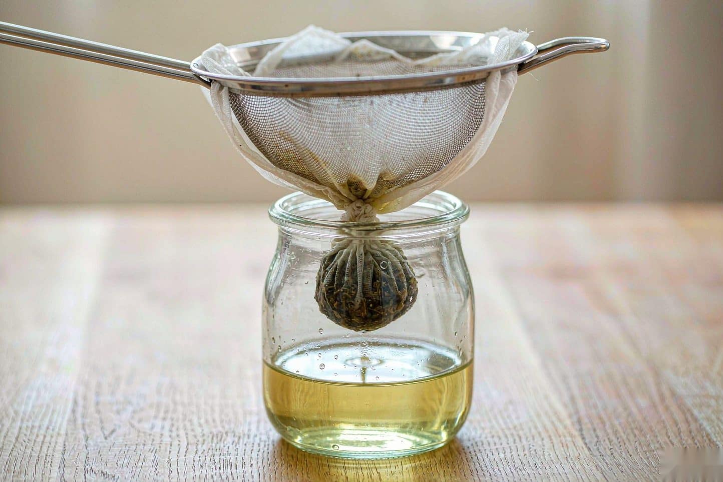 Warm cannabutter draining through cheesecloth in a mesh sieve into a glass jar