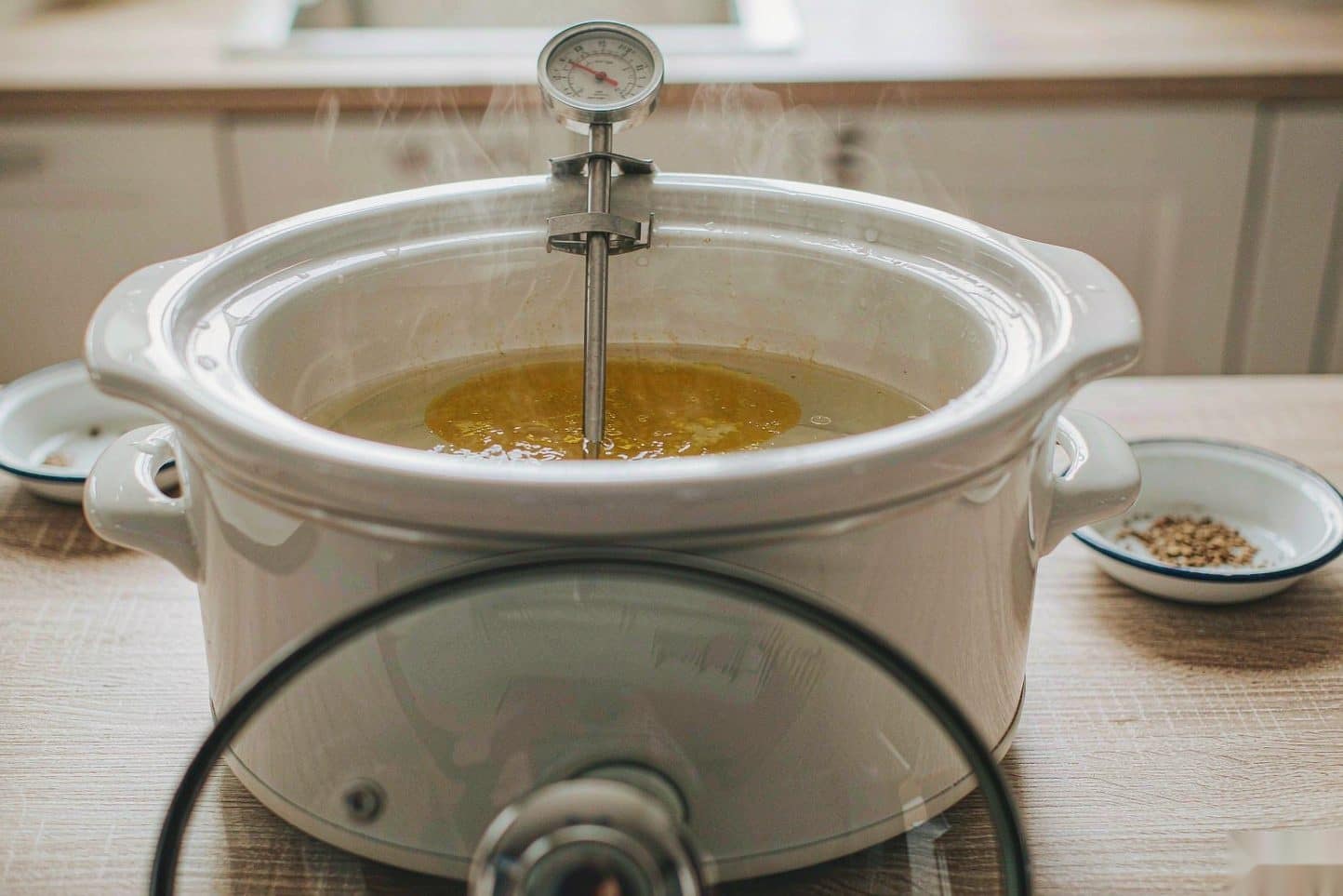 A slow cooker holding melted butter and water with a probe thermometer clipped to the rim